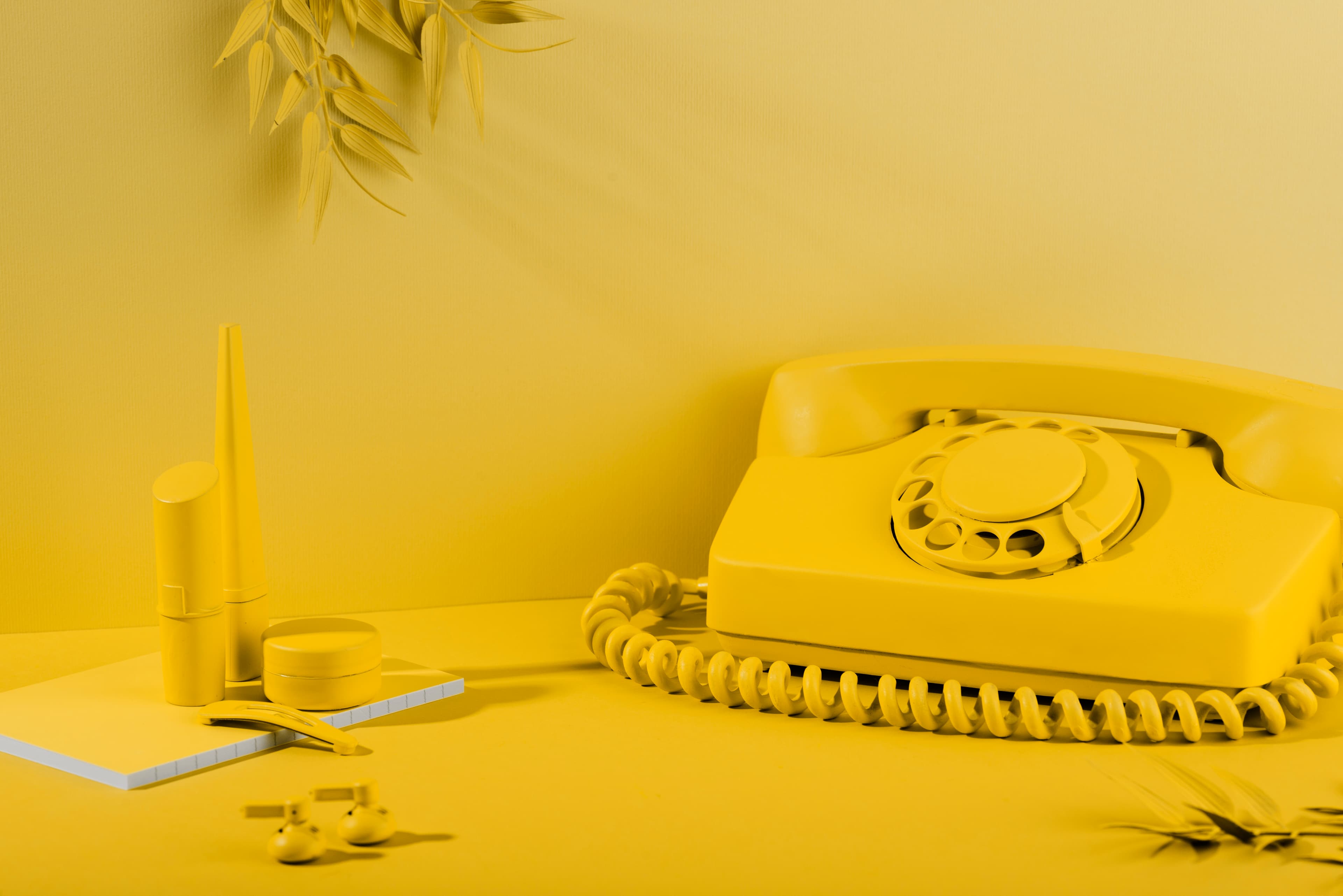 A monochrome yellow desk scene with a rotary telephone, notebook and stationery