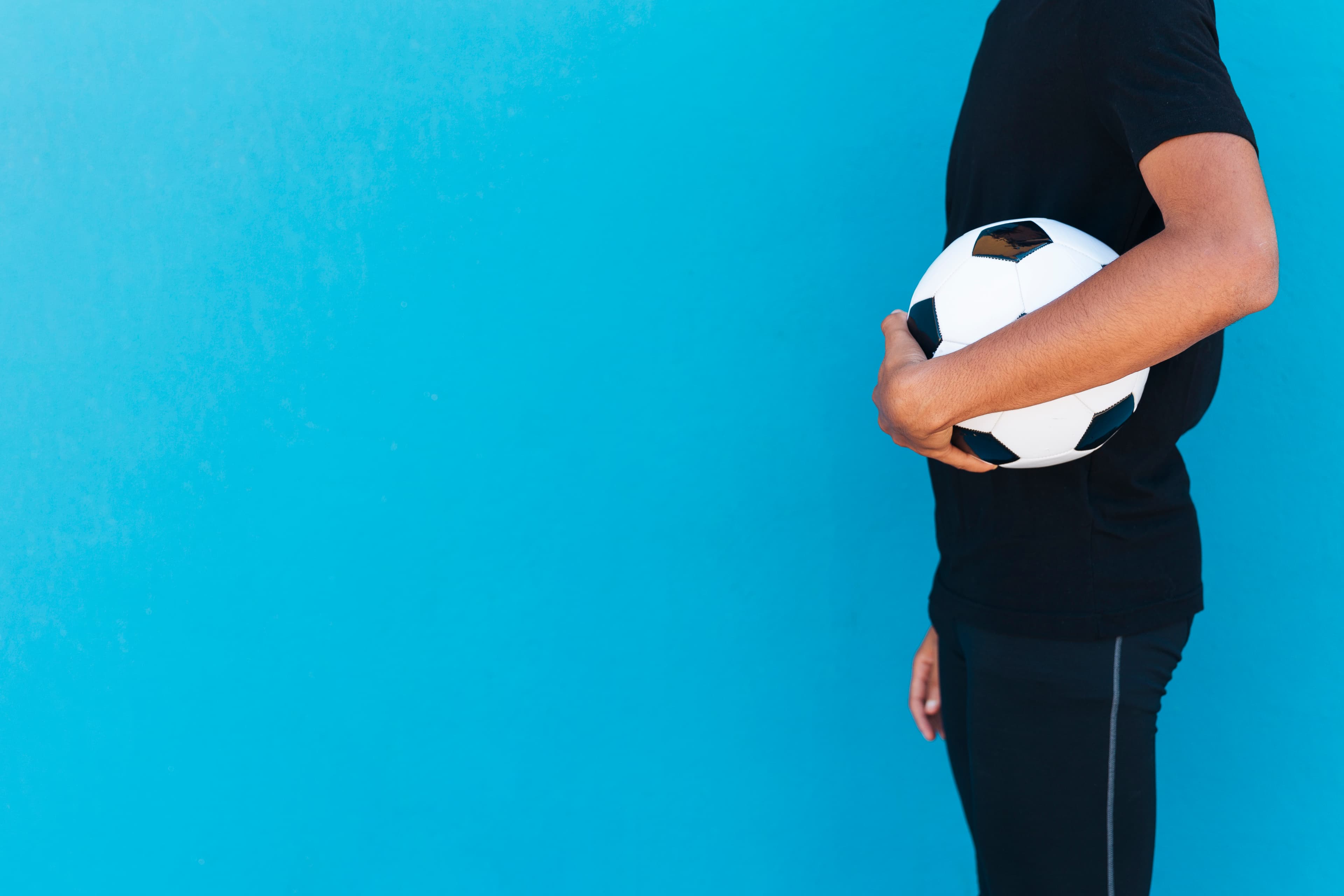 A footballer holding a football against a blue wall